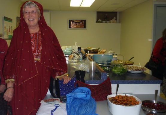 Twyla Gimbel with a display table of Afghan items: hand embroidered purses and pillow cases; burka; delicious rice dish served at all the weddings; pomegranates which grow very large and taste wonderful in Afghanistan.